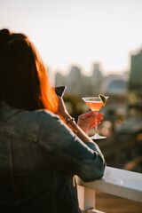 A girl takes a photo of a cocktail against the backdrop of a big city