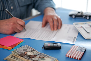 Close-up Of A Businessman Filling Car Sale Contract With Number Plate and Car Key Fob On Desk. Contract Paper Contains Placeholder Text. selective focus.