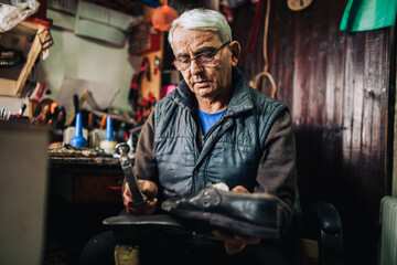 Obraz premium A senior artisan sitting at his shoemaker shop and fixing shoes.