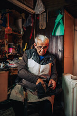 Obraz na płótnie Canvas A senior artisan is sitting at his cobbler workshop with boots in hands.