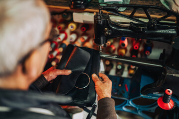 Top view of a senior cobbler repairing a purse in his shop.
