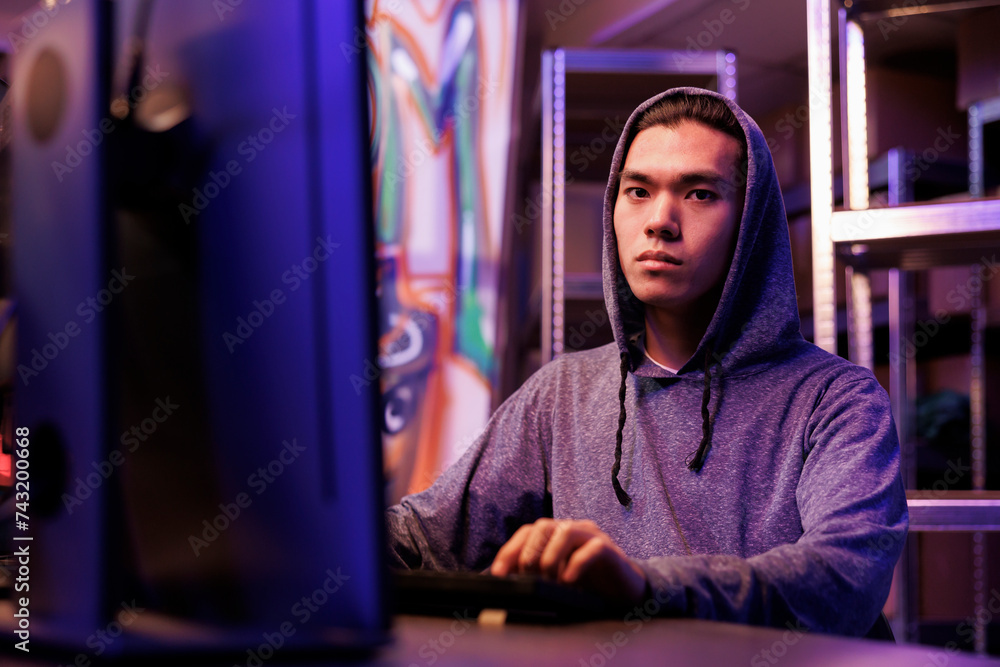 Poster young asian hacker doing ddos attack illegal activity on computer portrait. man in hood breaking law