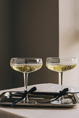 Two coupe glassed with sparkling wine decorated with satin ribbon bows standing on elegant silver...