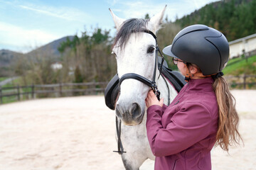 A serene moment as a young woman gently adjusts the bridle of her graceful white horse at the stable