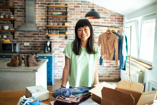 Smiling Asian woman packing clothes into a box at home