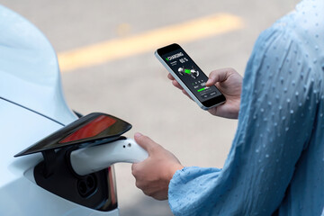 Hand insert EV charger plug into electric vehicle to recharge EV car, battery status display on...