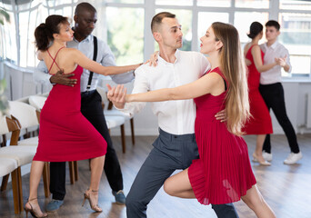 Fototapeta premium With unhurried music, guy and young woman in couple spins to rhythm of rumba during lesson for novice students. Classes in mini-groups for those who want to learn dancing