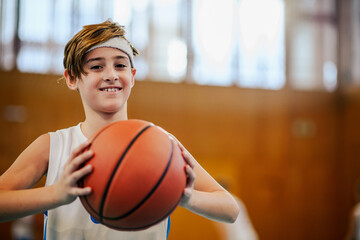 Portrait of a young basketball player standing on court with a ball.