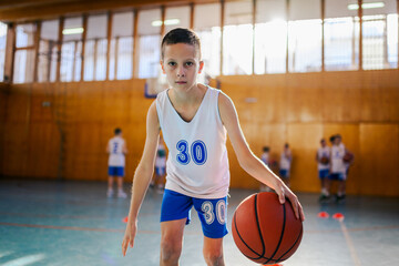 A young active athlete is dribbling a basketball on training at court.