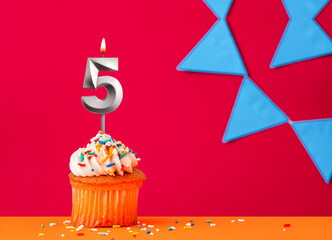 Birthday cupcake with candle number 5 on a red background with blue pennants