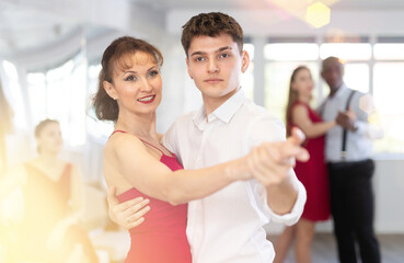 Confident handsome young Hispanic guy in formal wear learning to dance waltz with attractive female...