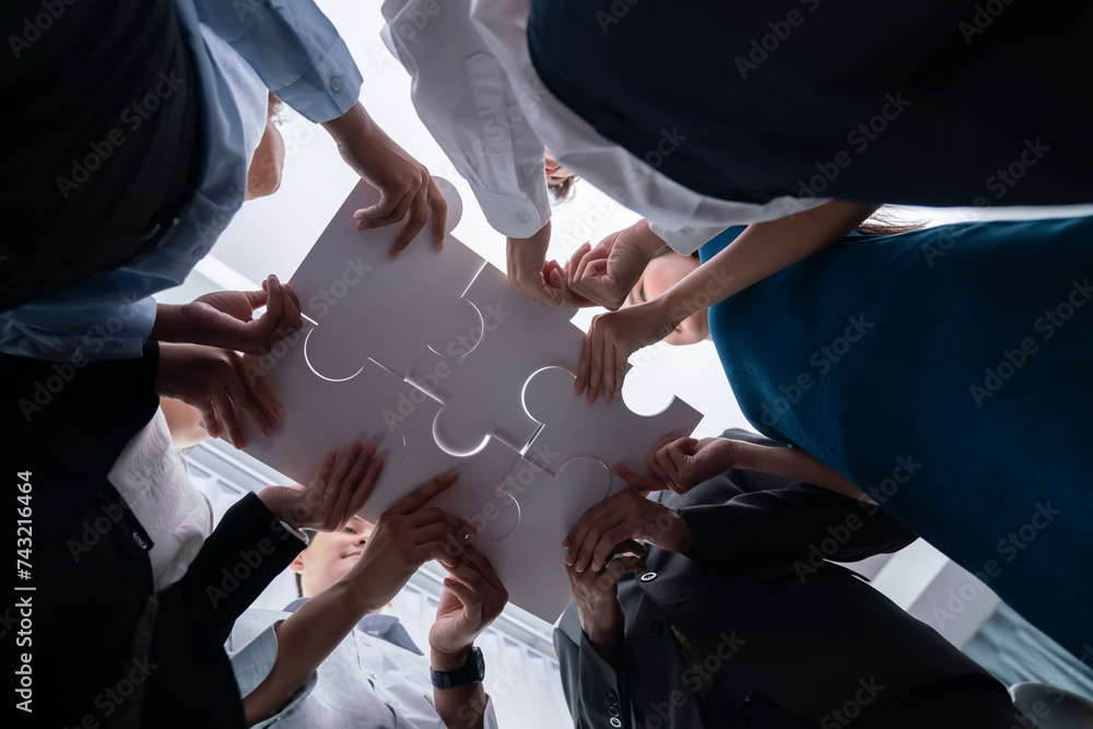 Poster below view of diverse corporate officer workers collaborate in office connecting puzzle pieces as pa