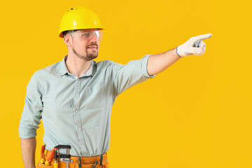 Male carpenter in safety goggles pointing at something on yellow background