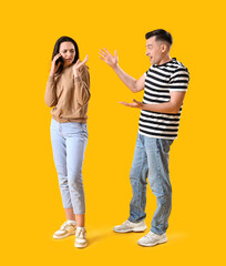 Fototapeta premium Young woman with mobile phone and her quarreling husband on yellow background