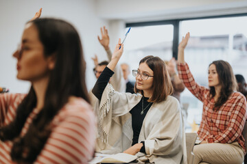 Active participation in education as young women in a bright classroom raise their hands to ask...