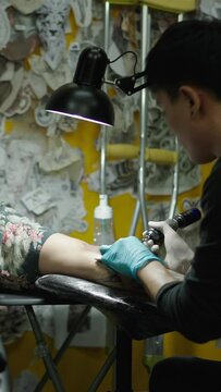 Asian tattoo artist making a tattoo to a lied down customer in a studio - Creative concept