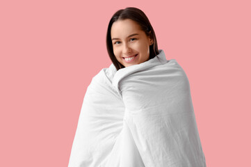 Fototapeta premium Pretty young woman wrapped in blanket on pink background