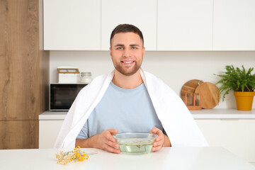 Young man doing steam inhalation at table in kitchen