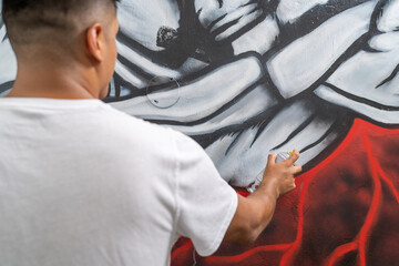Young male latin artist painting graffiti on wall indoors