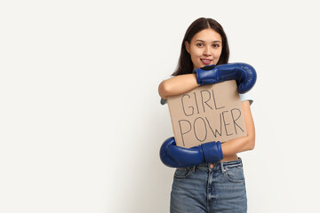 Young woman with sign GIRL POWER and boxing gloves on white background. Feminism concept