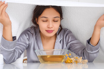 Young Asian woman doing steam inhalation at table in kitchen, closeup