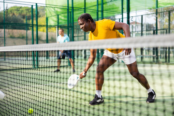 Sporty african american man playing padel tennis outdoor court