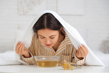 Young Asian woman doing steam inhalation at table in bedroom