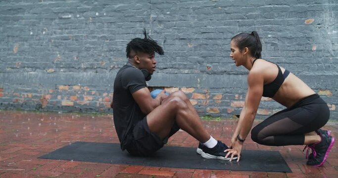 Rain, exercise ball and people doing crunches in outdoor partner workout, fitness or core muscle building. Winter season, support and couple of friends exercise, hard work and training abs on ground