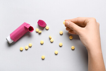 Child's hand with asthma inhaler and pills on white background