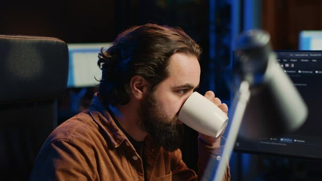 Computer scientist drinking cup of coffee while developing code on PC using java programming languages. IT admin brainstorming ways of fixing database errors, enjoying hot beverage, camera A