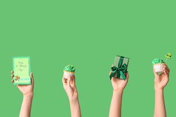 Female hands with tasty cupcakes, gift box and festive postcard for St. Patrick's Day on green...