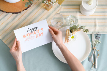 Female hands with greeting card and beautiful table setting for International Women's Day...