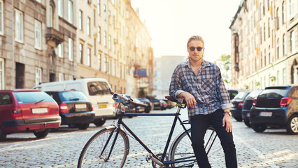 Living in the city, portrait of young man. Young man sitting on the luggage rack of his bicycle in...