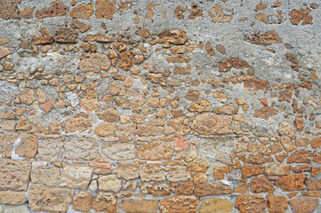 Very old stone wall in irregular pattern with stones in different shades of brown and masonry mortar, background