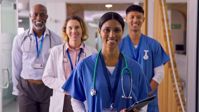Camera tracks across multi-cultural medical team in modern hospital corridor smiling into camera - shot in slow motion