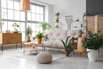 Interior of light modern living room with sofa, table, houseplants, shelving unit, wooden chest...
