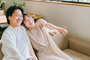 家のリビングのソファに座る仲良しの若い日本人夫婦（スキンシップ）
