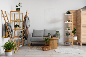 Interior of cozy living room with shelving units, houseplants, table and sofa