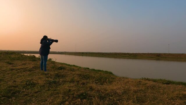A female photographer taking photo of water birds at a lake near Bakkhali sea beach.