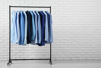 Dry-cleaning service. Many different clothes hanging on rack near white brick wall, space for text