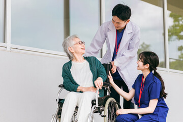 病院・介護施設にいる車椅子に乗った高齢者と医師・看護師
