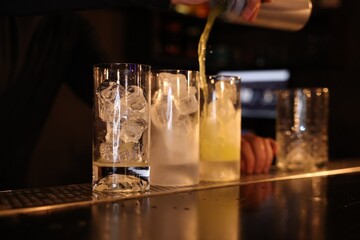 Bartender pouring energy drink into glass at counter in bar, selective focus