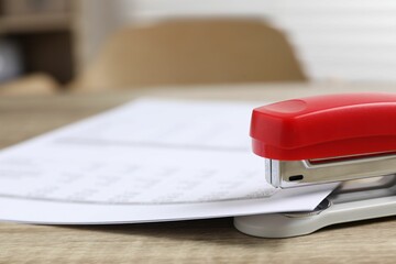 Bright stapler with documents on wooden table indoors, closeup