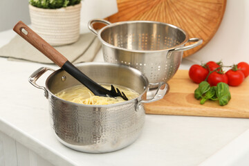 Cooked spaghetti and pasta server in metal pot on white countertop