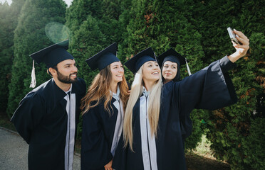 Happy students in graduation caps and gowns celebrating their achievement, taking selfies and...