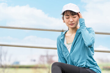 ランニング・ウォーキング中に頭痛・偏頭痛で困るスポーツウェアのアジア人女性
