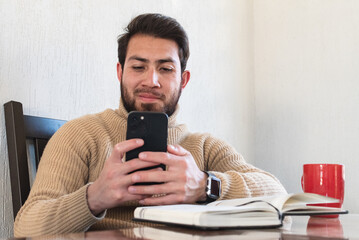 Joven apuesto con suéter y barba usando su teléfono celular para comunicarse 