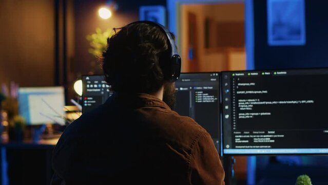 Engineer wearing headphones while using coding to fortify security, remotely working for IT company. Software expert listening music and upgrading binary code scripts on computer, camera A