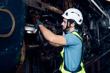 Male engineer maintenance locomotive engine wearing safety uniform, helmet and gloves work in locomotive repair garage.