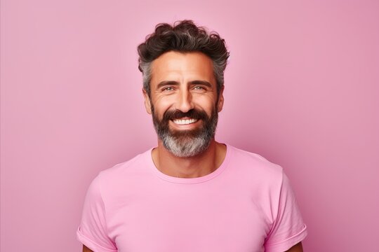 Handsome bearded man in casual t-shirt looking at camera and smiling while standing against pink background